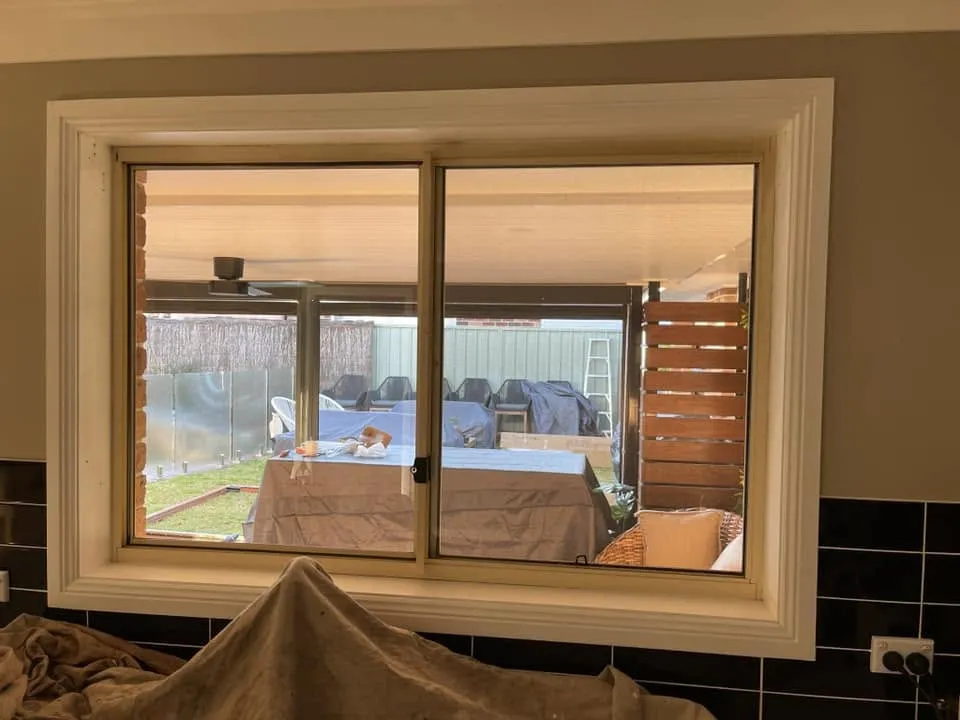 New white sliding window fitted in a kitchen wall during renovation, with the patio beyond