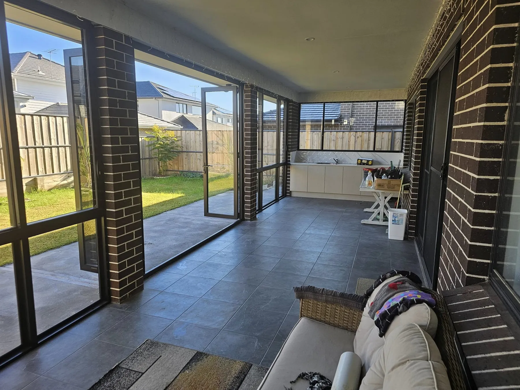 Tiled alfresco room enclosed by black-framed glass panels between brick piers