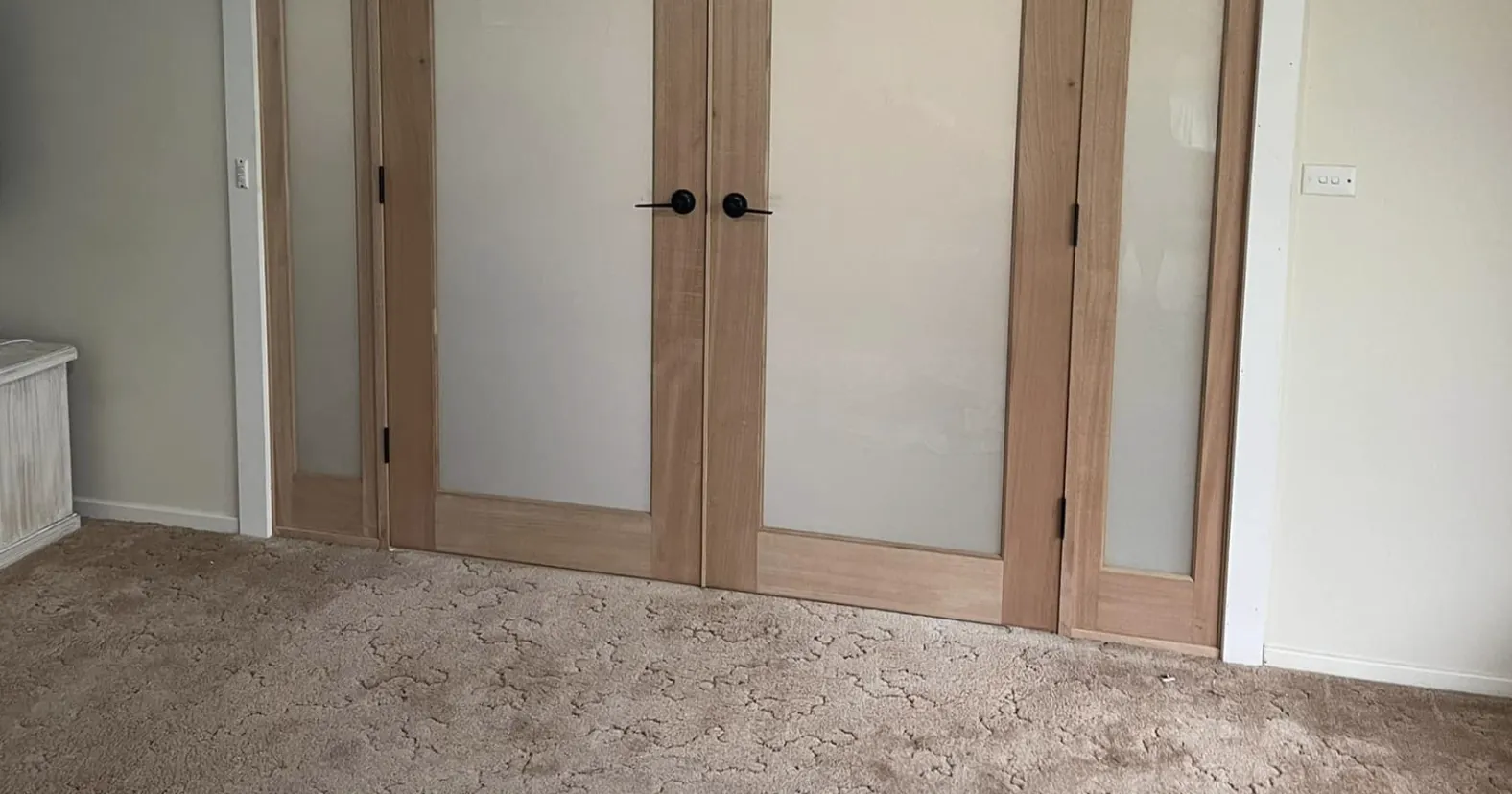 Closed timber French doors with frosted glass panels and matching sidelights in a carpeted room