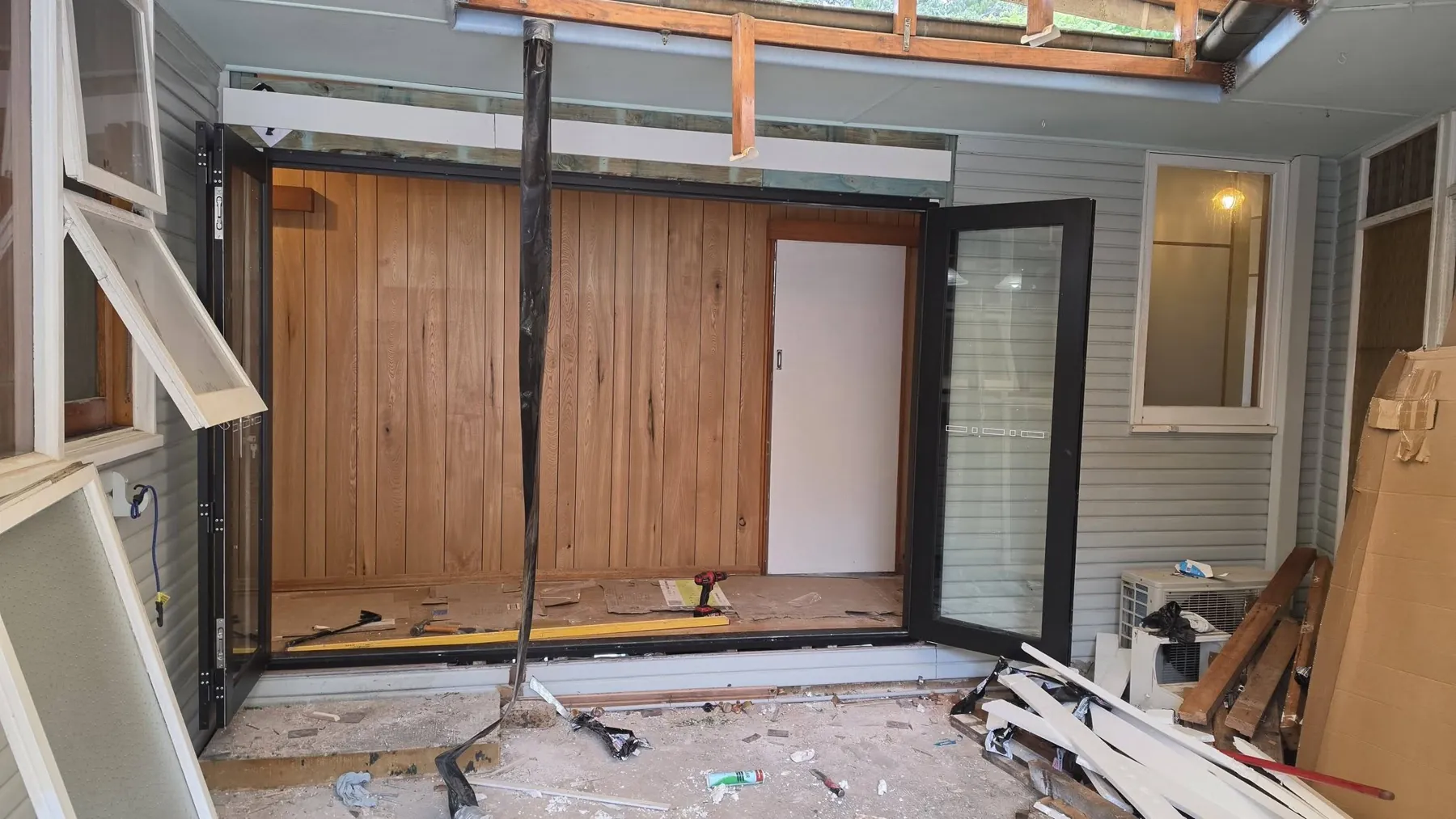Timber cladding panel and door framing being fitted in an open patio wall