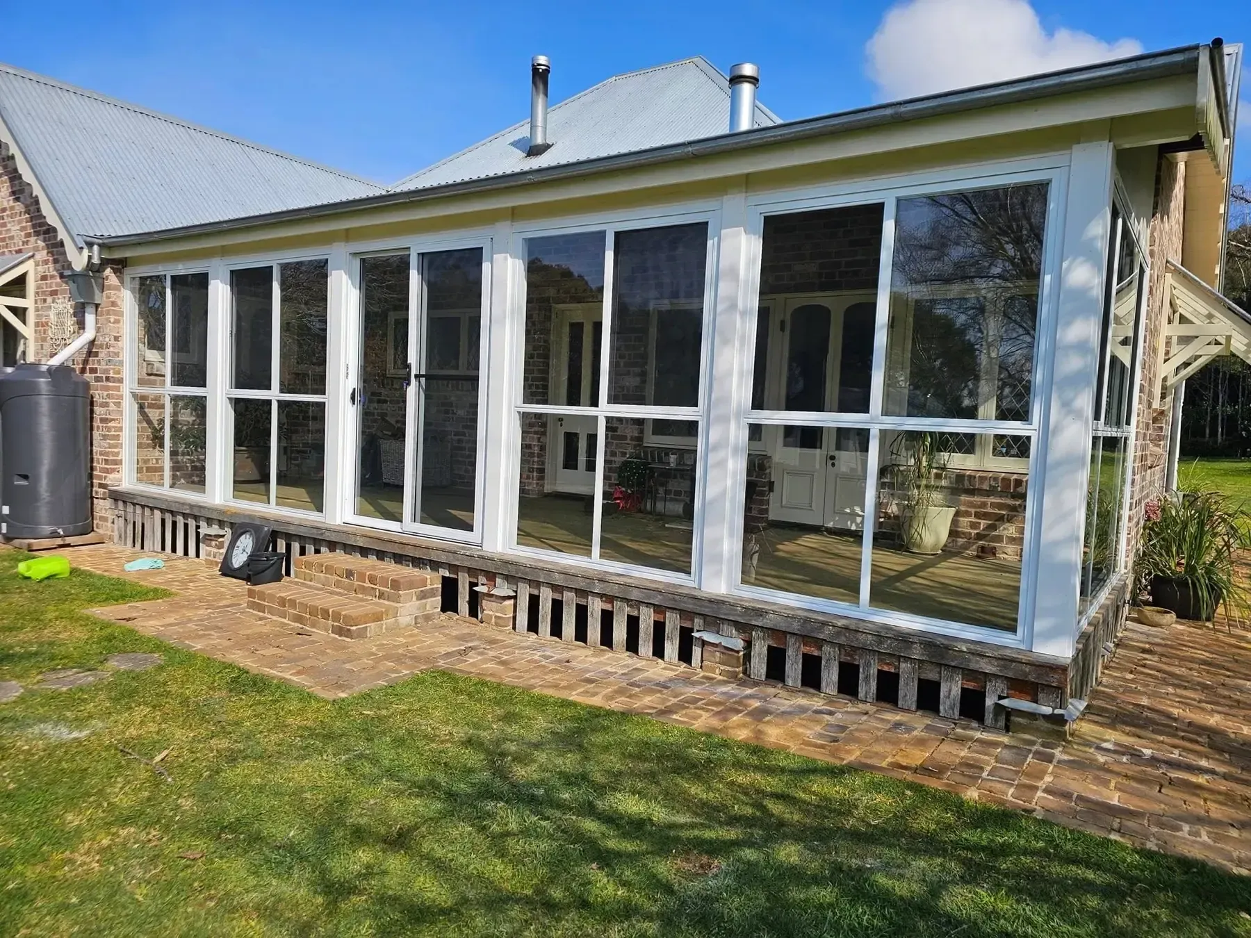 Enclosed verandah sunroom with white-framed windows and doors on a brick base