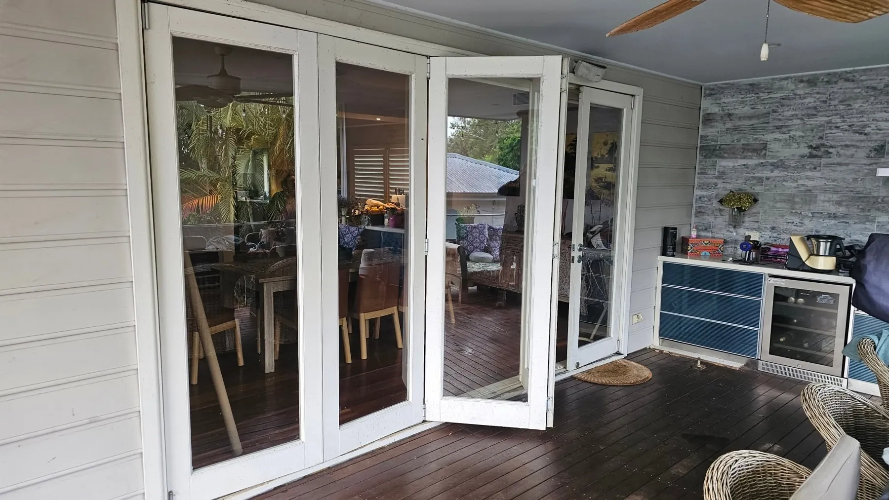 White timber bifold doors partly open from a deck into a dining room