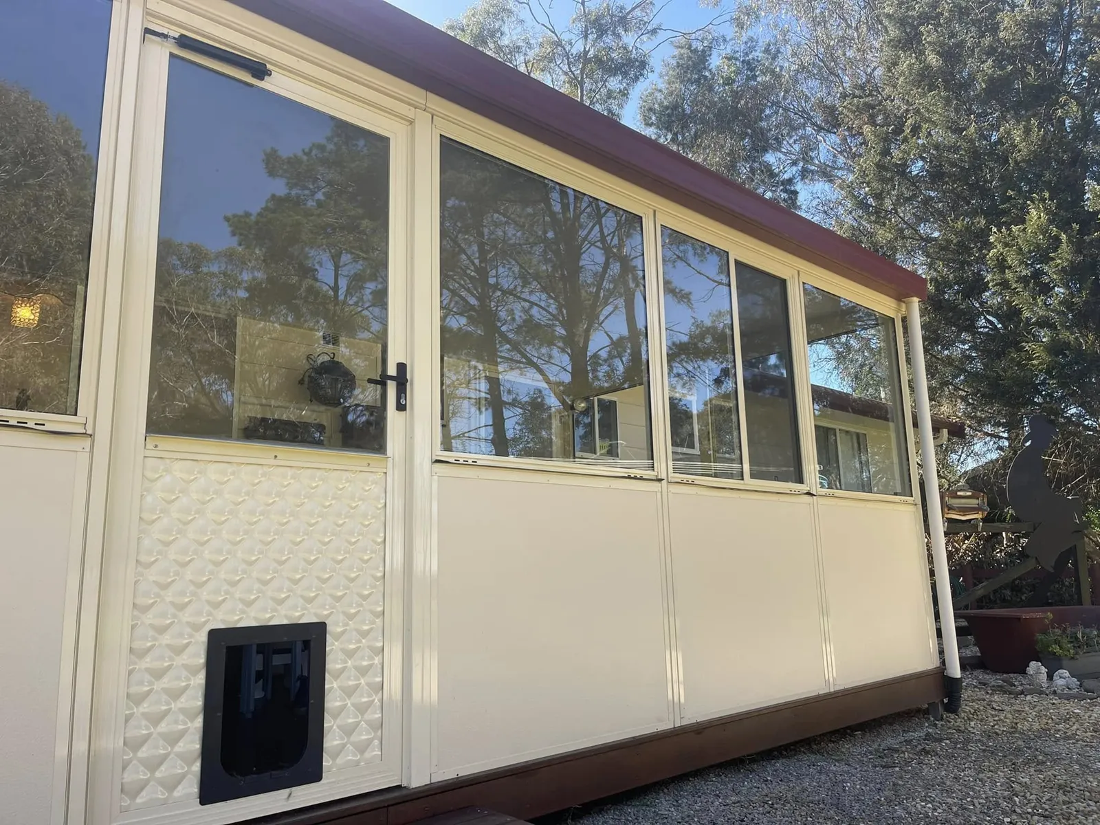 Cream alfresco enclosure with a row of glass windows, a glass door and a pet door