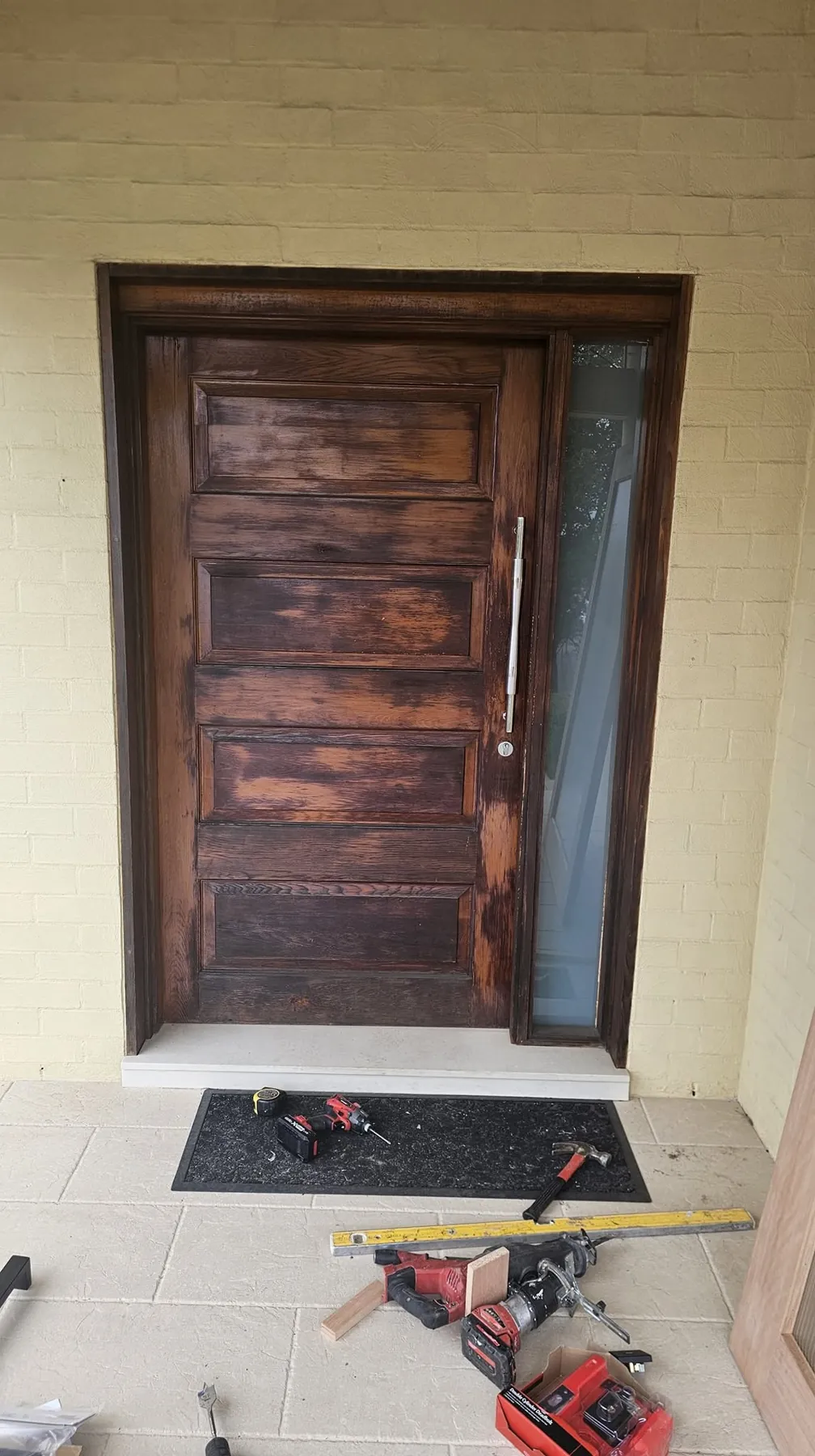 Stained timber front door with a side light, tools laid out on the tiled entry