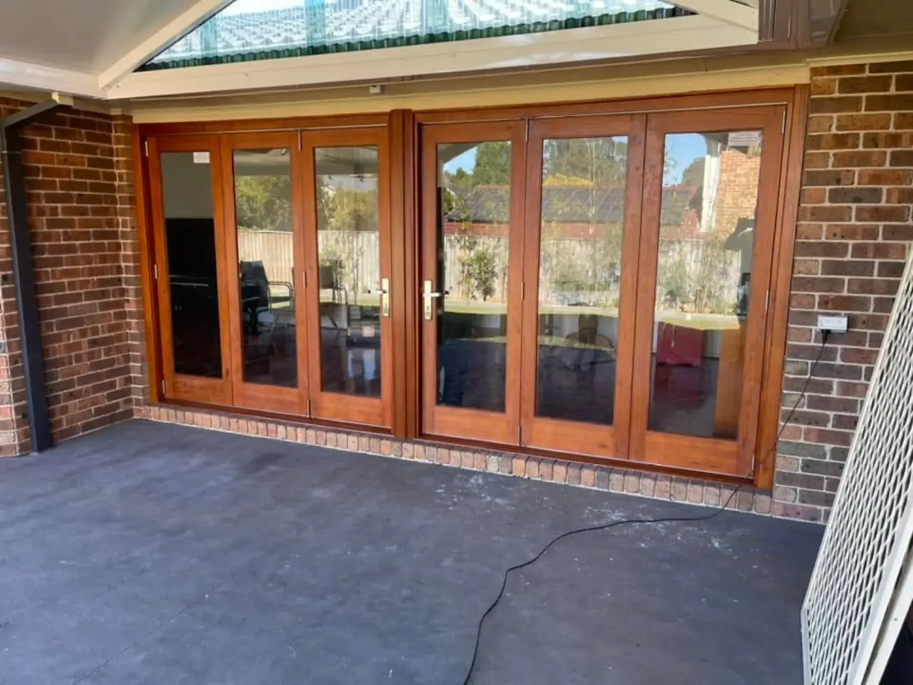 Timber bifold doors fitted across a brick patio wall under a covered pergola