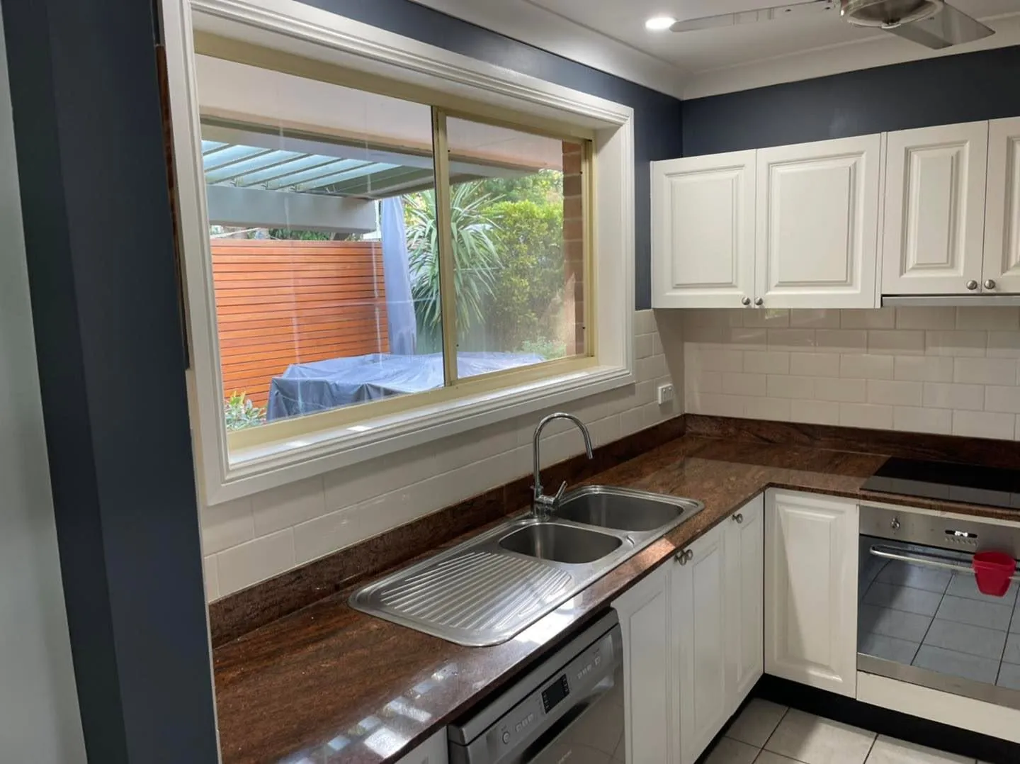 White-framed sliding window above a kitchen sink looking out to a covered patio