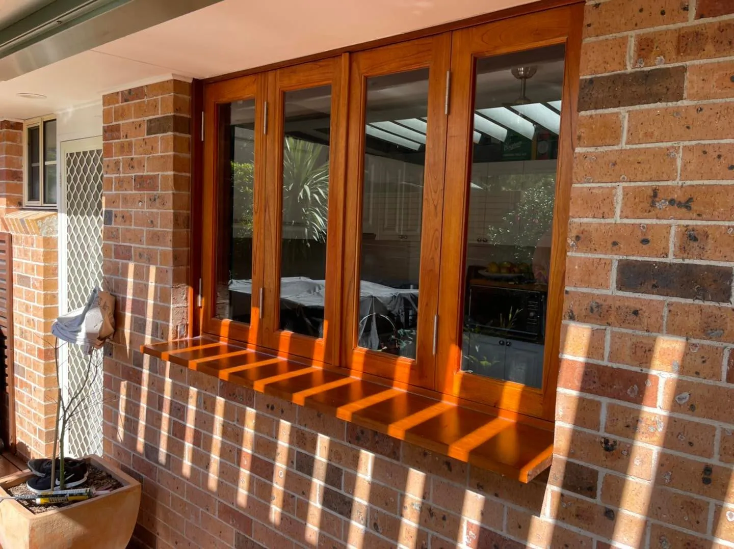 Stained timber bifold servery window set into a brick wall beside an alfresco area