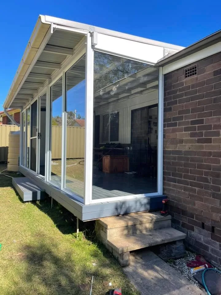 White aluminium glass sunroom enclosure on a raised deck beside a brick home in the Southern Highlands