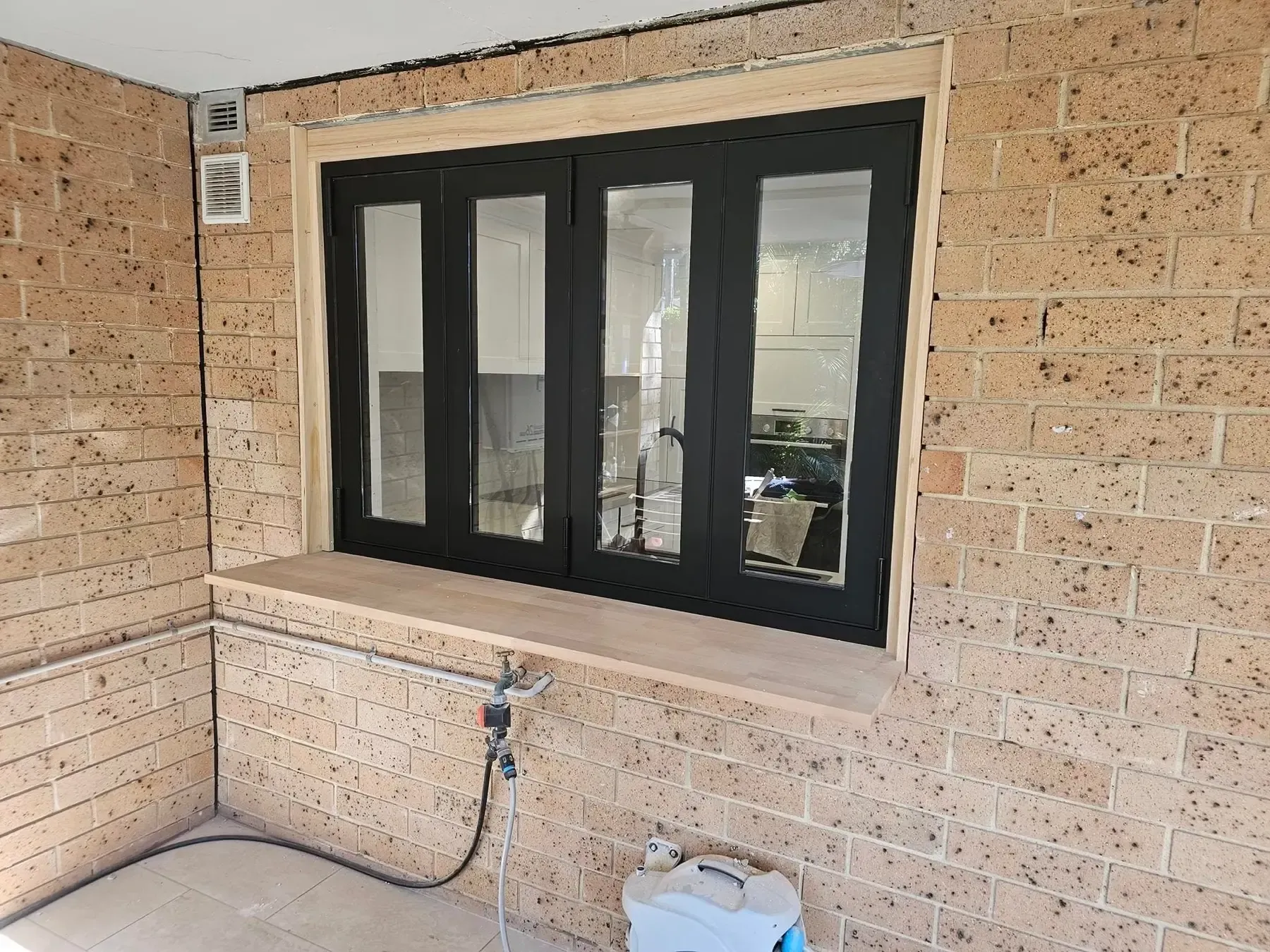 Black aluminium bifold window installed in a sandstone-coloured brick wall